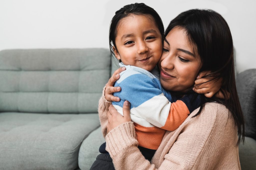 Happy Latin American mother and child son hugging each other at home - Family love concept